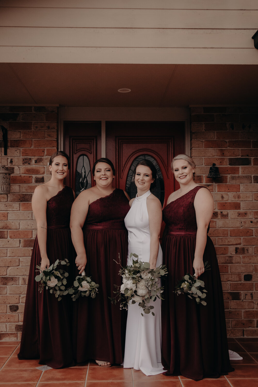 Bridesmaids in burgundy one-shoulder lace gowns with halter-neck bride, altered at Jacqui's Shoalhaven Heads studio