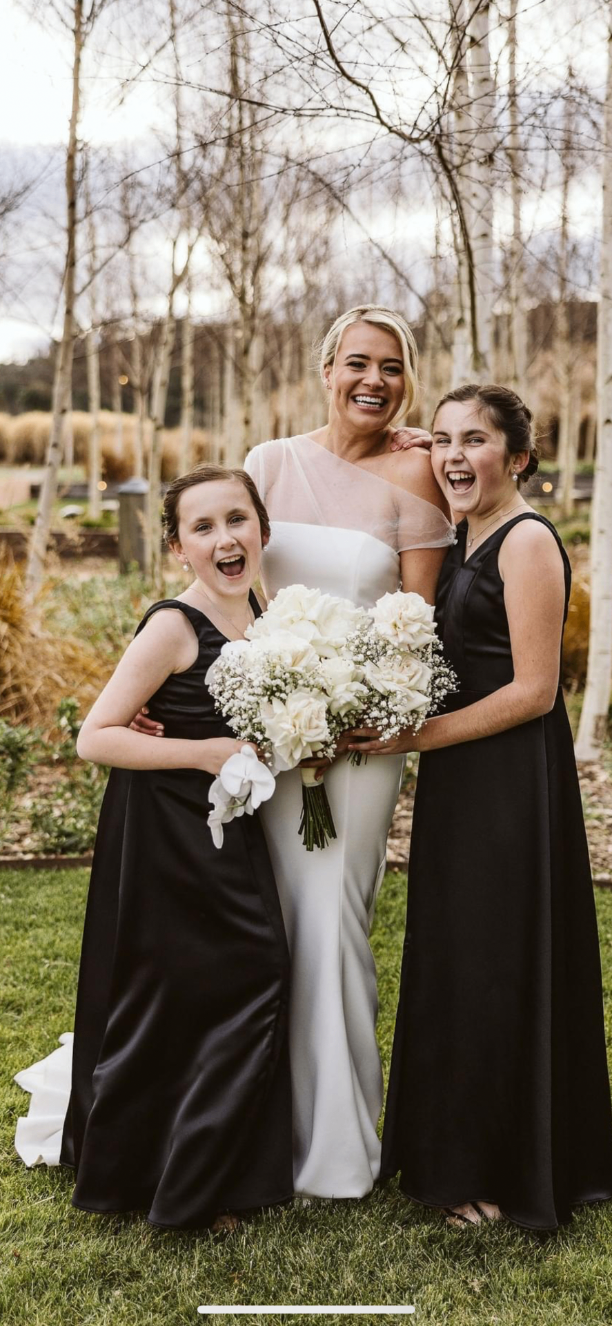 Bride in white with bridesmaids and flower girl in black gowns outdoors, altered by Jacqui
