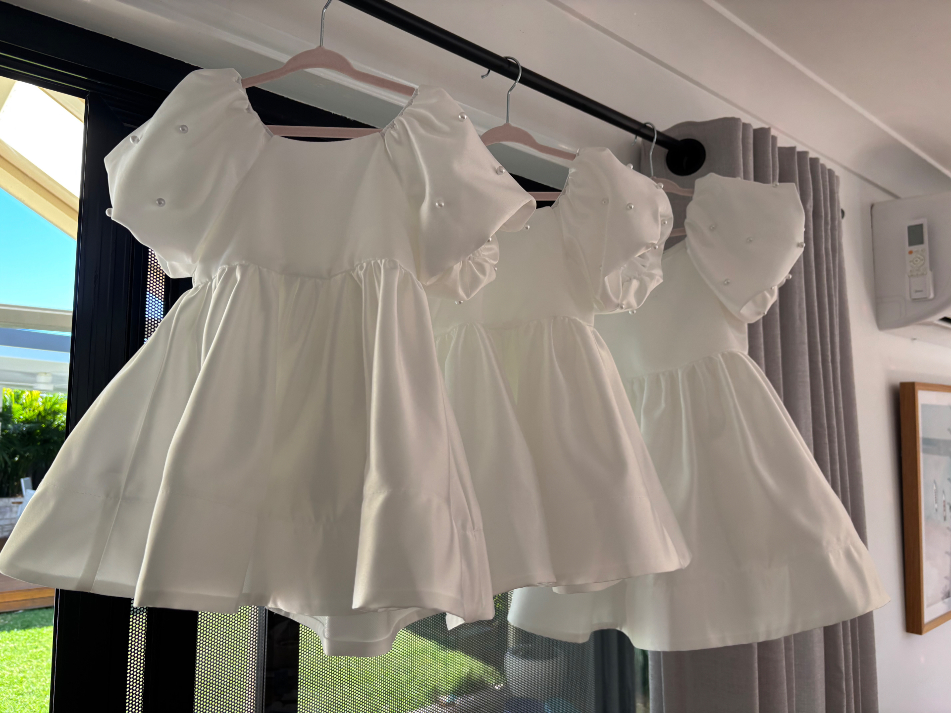 Three matching ivory satin flower girl dresses with pearl detailing on hangers