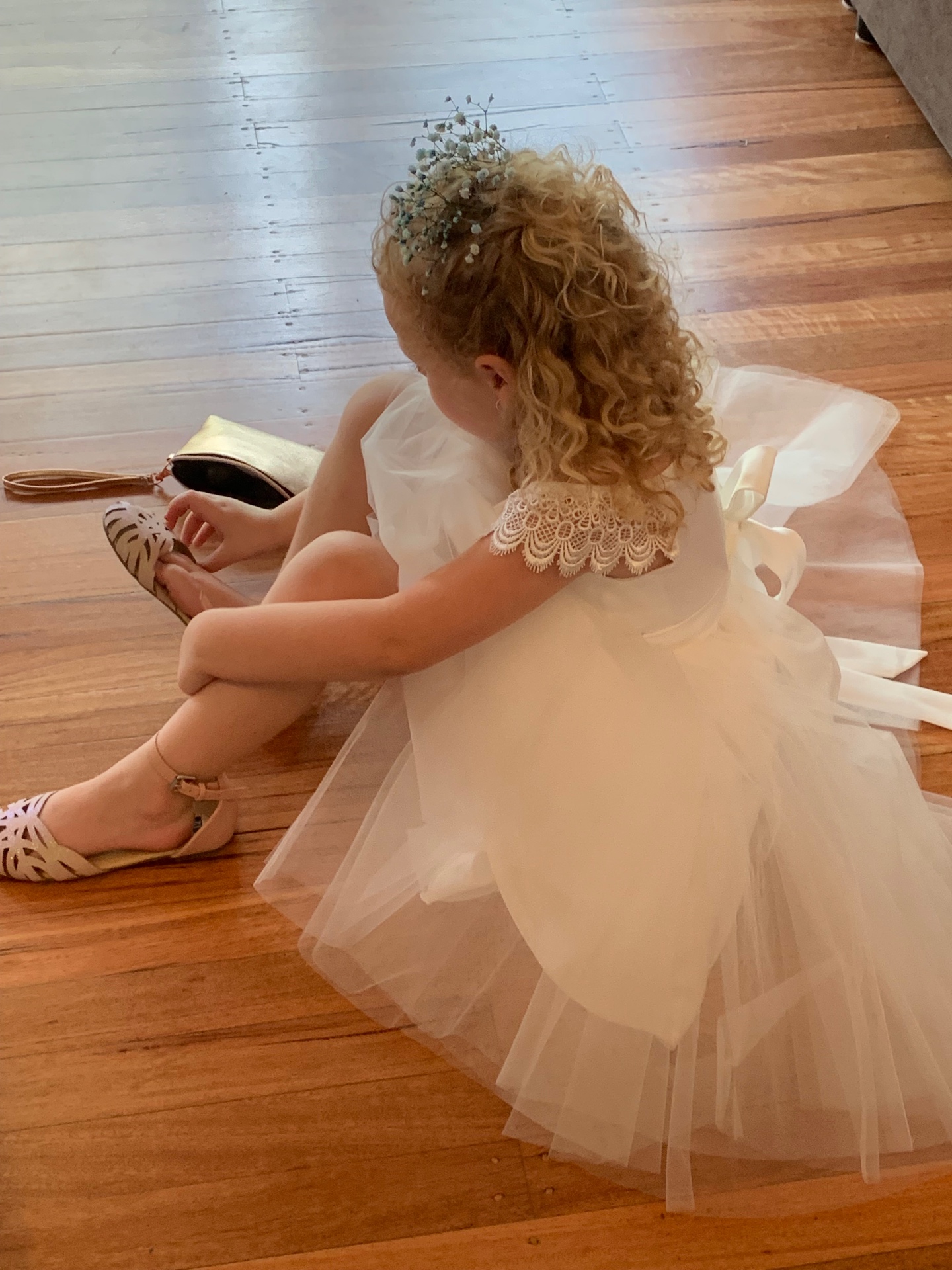 Flower girl in ivory tulle dress with lace bodice and baby's breath hair piece, seated on timber floor